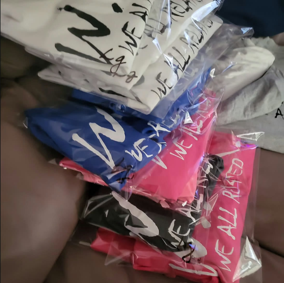 Stack of W.A.R. shirts in white, blue, pink and black, freshly packaged